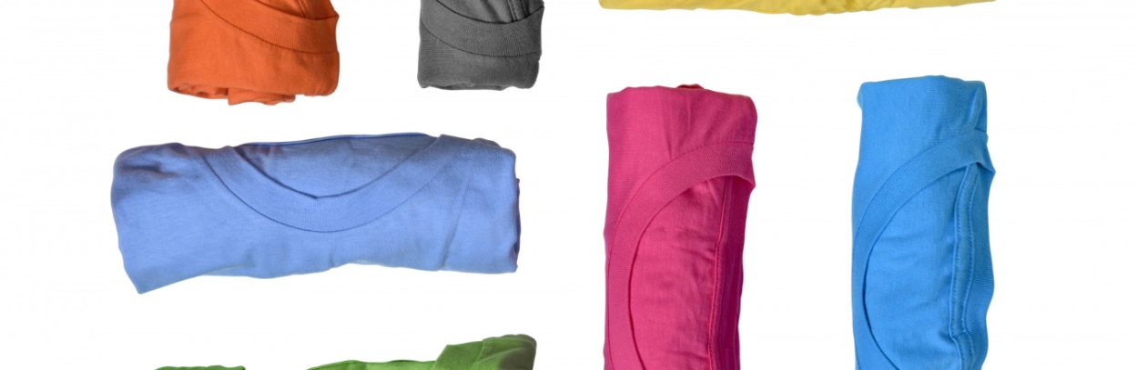 Rolled up multi-colour T-shirts arranged neatly, ready for custom printing as branded T-shirts.