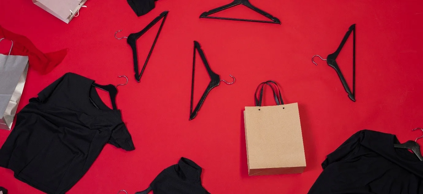 Black hangers, a black corporate T-shirt, and a gift bag scattered on a vibrant red surface, highlighting branded apparel and packaging.