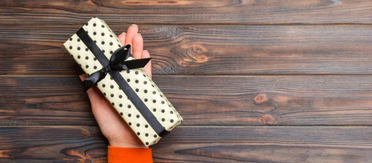 Hand holding a small white spotted corporate gift box tied with a black ribbon, representing personal and thoughtful business gifting.